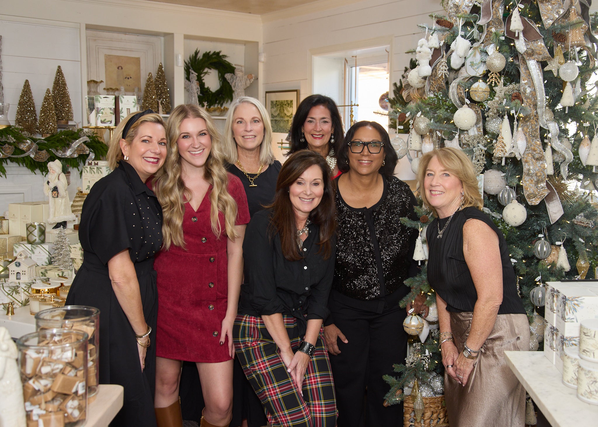 Group of women posing for a photo in a decorated room with Christmas trees and holiday decor.