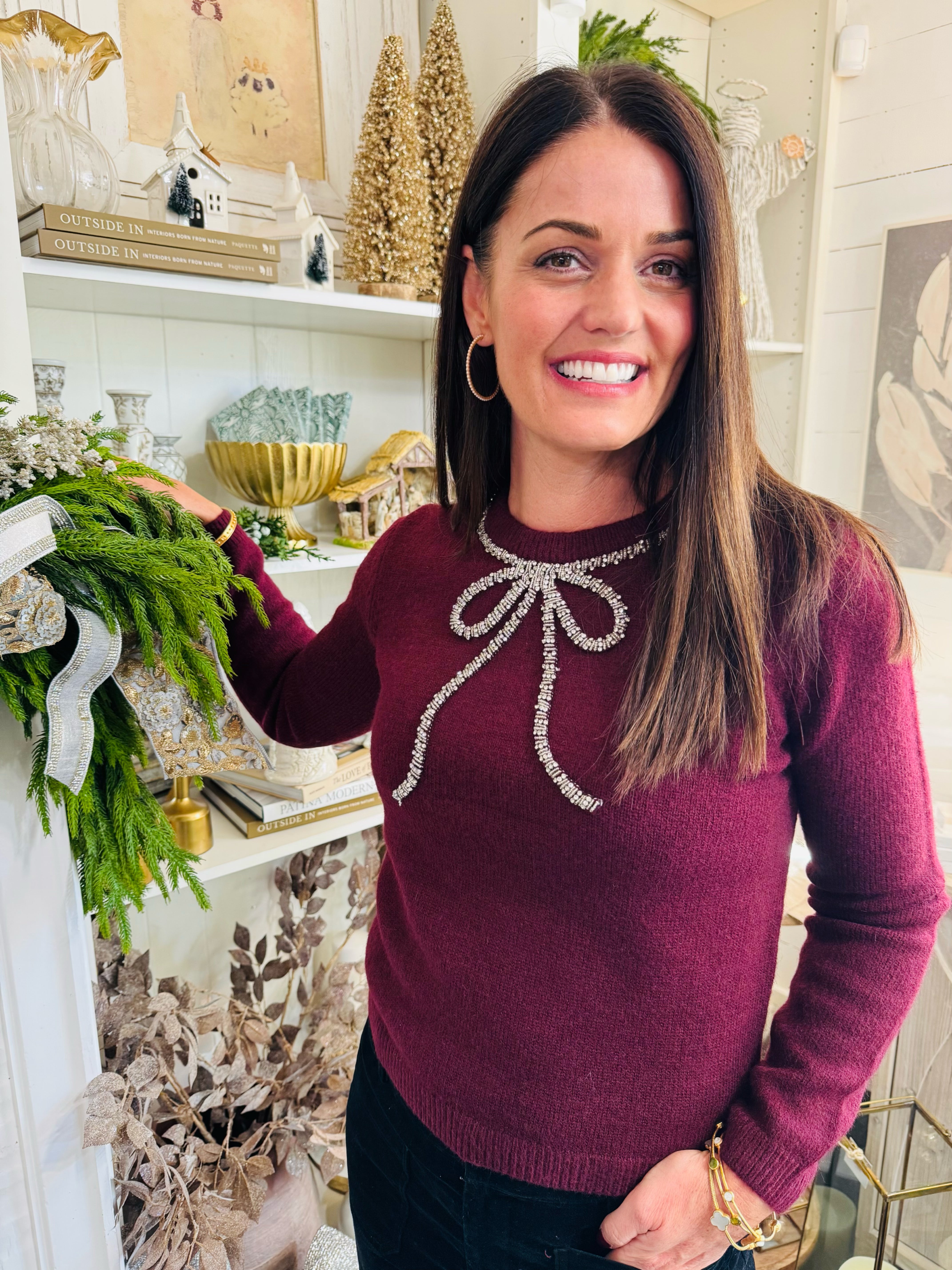 Woman wearing a burgundy sweater with a decorative bow in a decorated room.